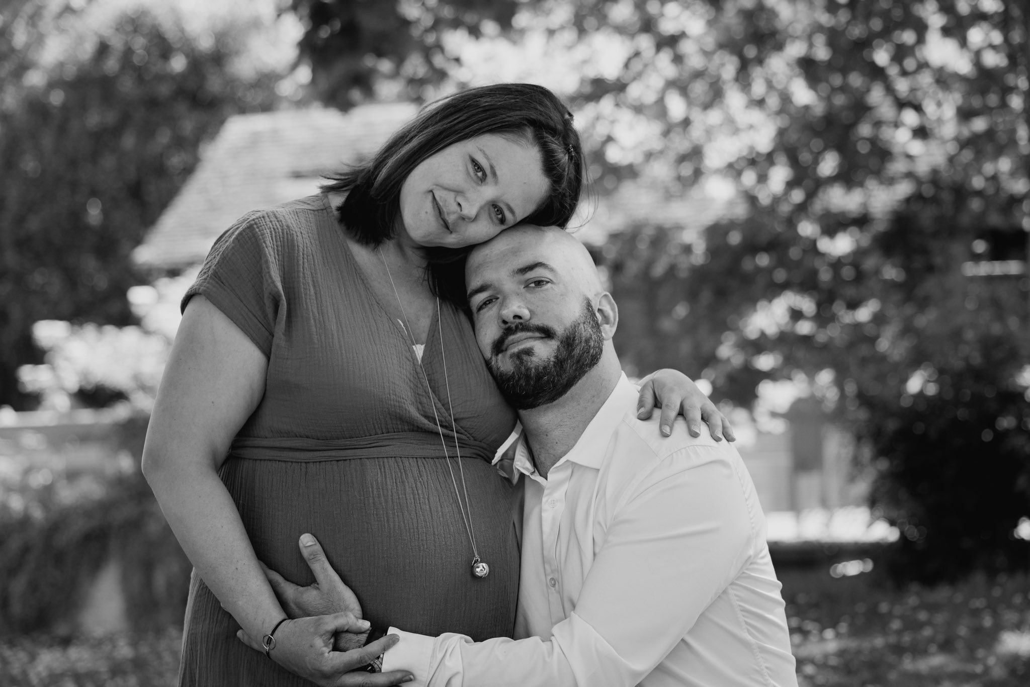 Couple attend un enfant, posé tendrement en extérieur, main sur le ventre de la future mère.