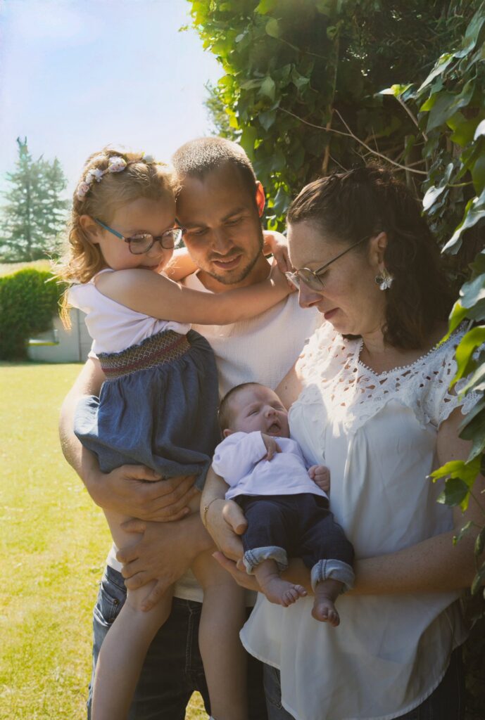 Famille de quatre personnes réunie dans un jardin ensoleillé, deux adultes tenant chacun un enfant.